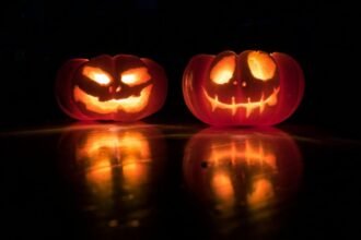 Two glowing carved pumpkins reflected on a dark surface, illustrating a guide to Halloween in London and planning a safer night out
