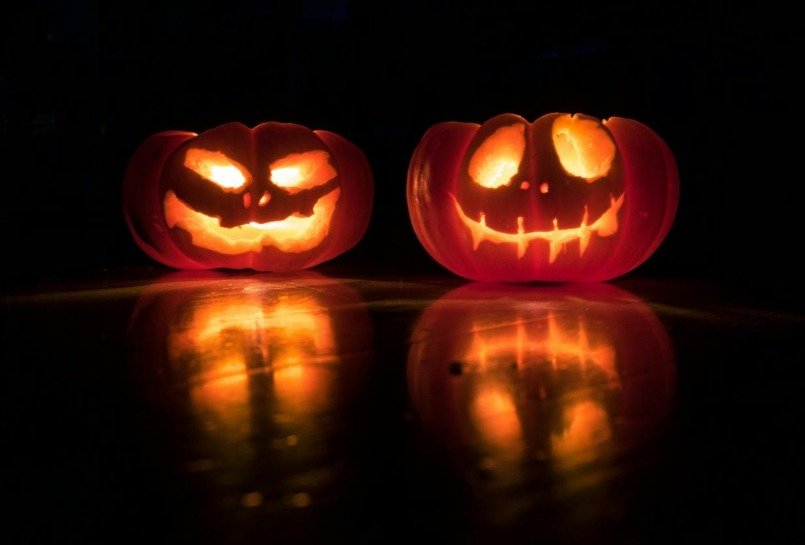 Two glowing carved pumpkins reflected on a dark surface, illustrating a guide to Halloween in London and planning a safer night out